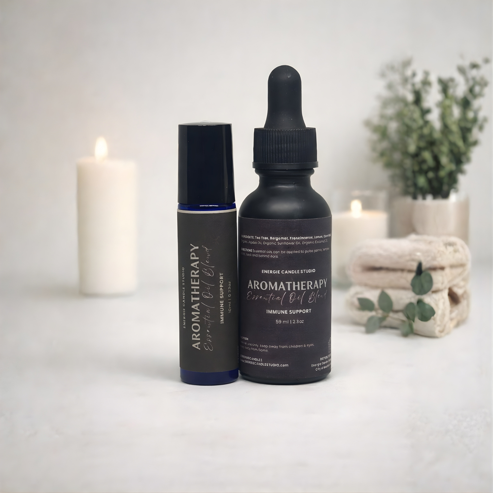 Two aromatherapy essential oil bottles on a white surface with candles and plants in the background.