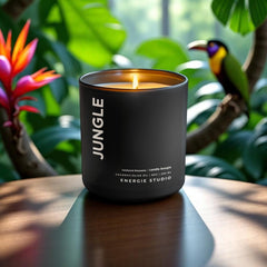a black candle with a cotton wick set on a brown wood table with a jungle background