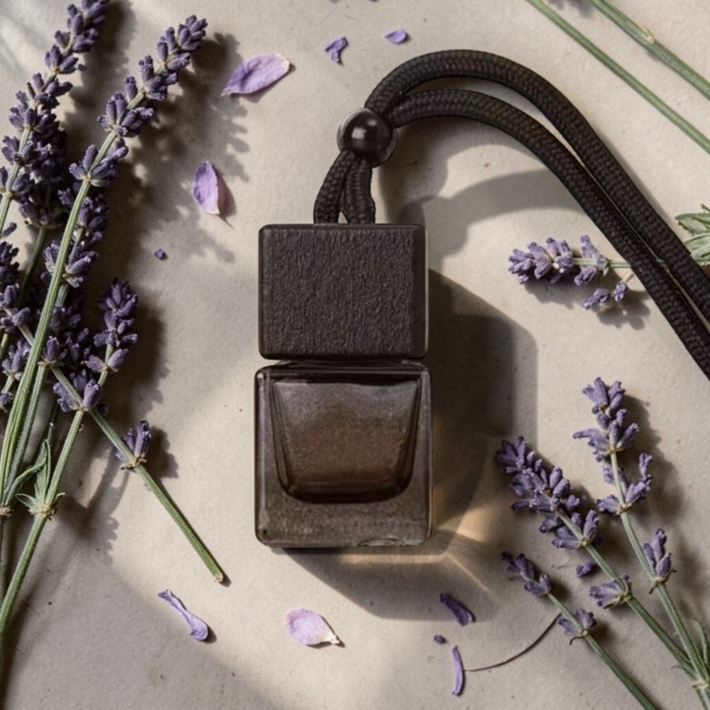 Dark brown square perfume bottle with a black strap on a light surface with lavender flowers.