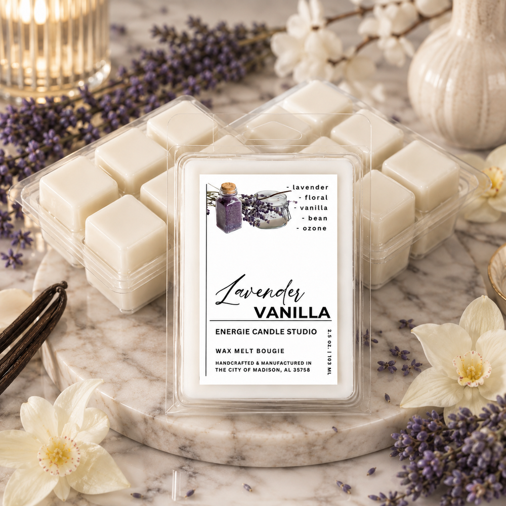 A clear plastic clamshell package of wax melt bougie cubes sits on a marble slab with lavender sprigs, white flowers, and a vanilla bean around it. The front label reads 'Lavender Vanilla' and 'Energie Candle Studio.