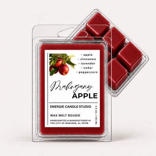 Two clear plastic clamshell packages of wax melt candles on a light gray studio background. The front package shows a red wax melt tray with a white label reading 'Mahogany APPLE' and 'ENERGIE CANDLE STUDIO'; a second package sits behind it showing additional red wax cubes.