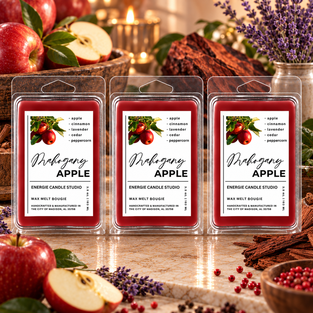 Three packaged wax melts labeled 'Mrhegan APPLE' are arranged on a tabletop with red apples, cinnamon sticks, lavender, and candles in the background, creating a warm autumnal scene.