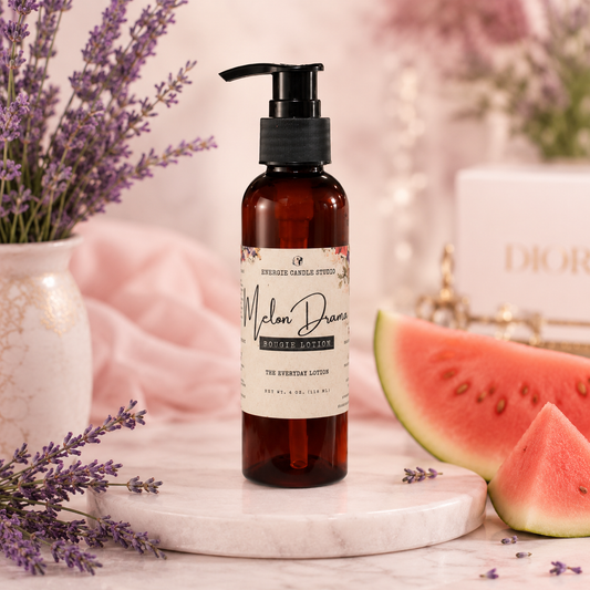 A bottle of Rosemary Creek Cosmetics Melon Dream Moisturizing Lotion stands on a white marble slab. The scene is styled with watermelon slices, lavender sprigs in a vase, and a soft pink fabric backdrop, with a Dior box blurred in the background.