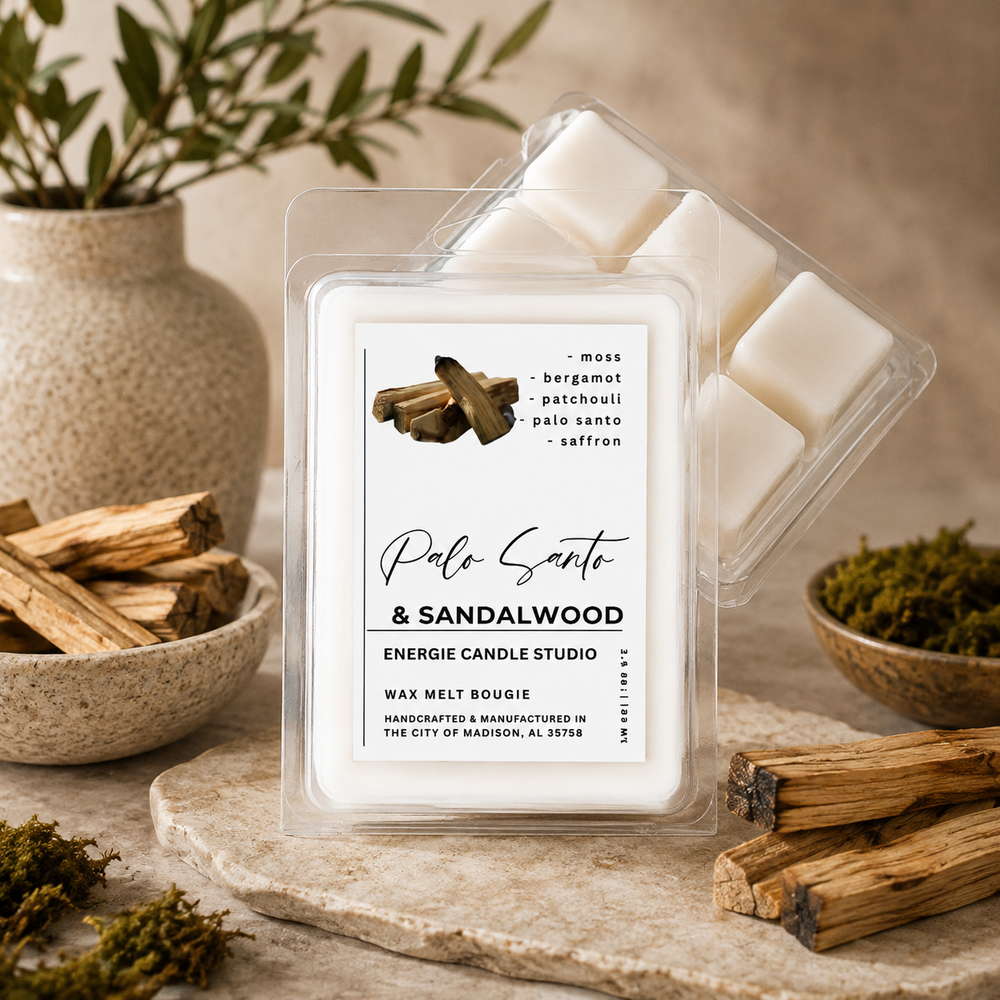 A wax melt package labeled 'Palo Santo & Sandalwood' by Energie Candle Studio, shown with clear plastic clamshell packaging and white wax cubes. The product is styled on a stone surface with wood bundles, moss, and a vase in the background.
