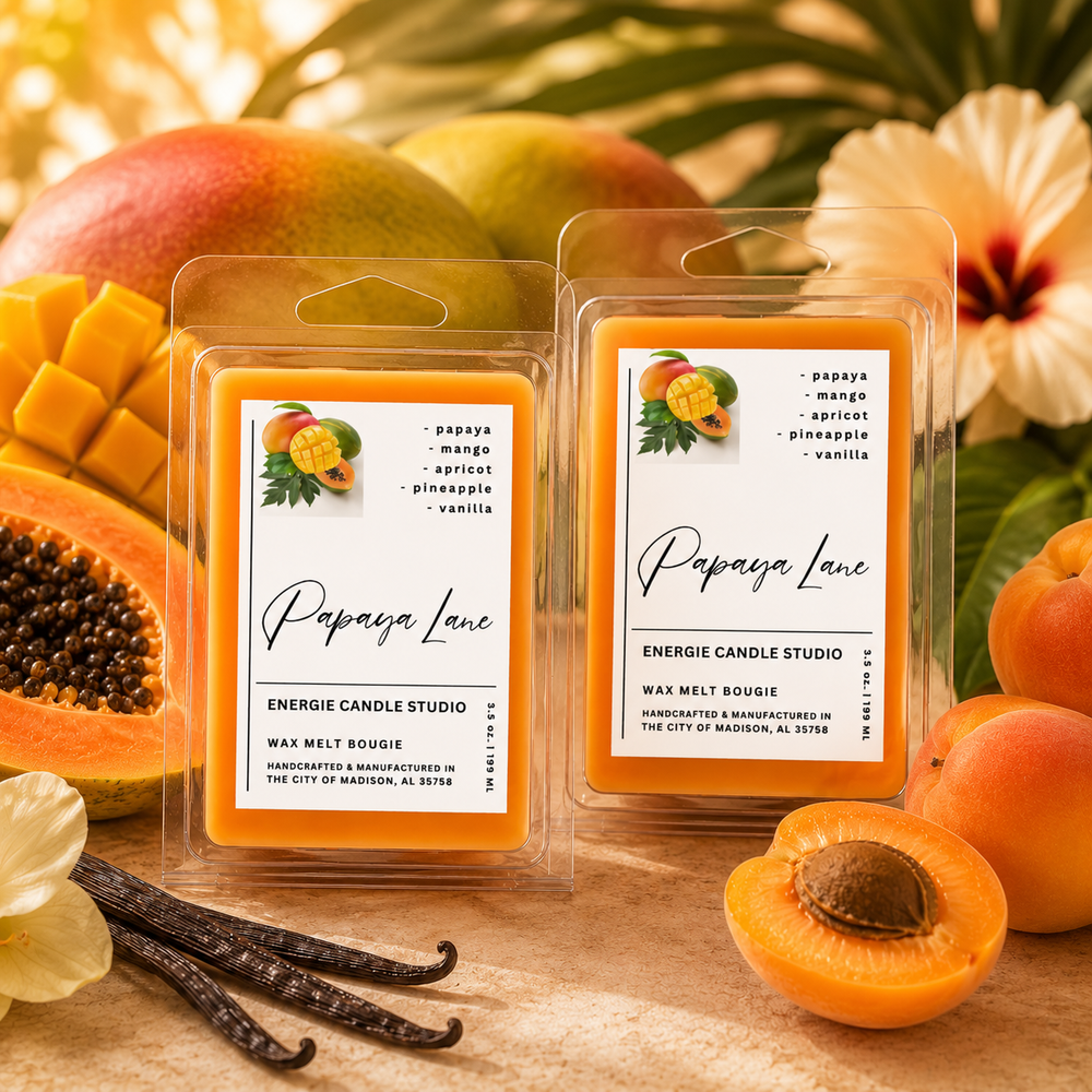 Two packaged wax melt products labeled Papaya Lane by Energie Candle Studio, surrounded by fresh papaya, mango, vanilla beans, and tropical flowers on a wooden surface.