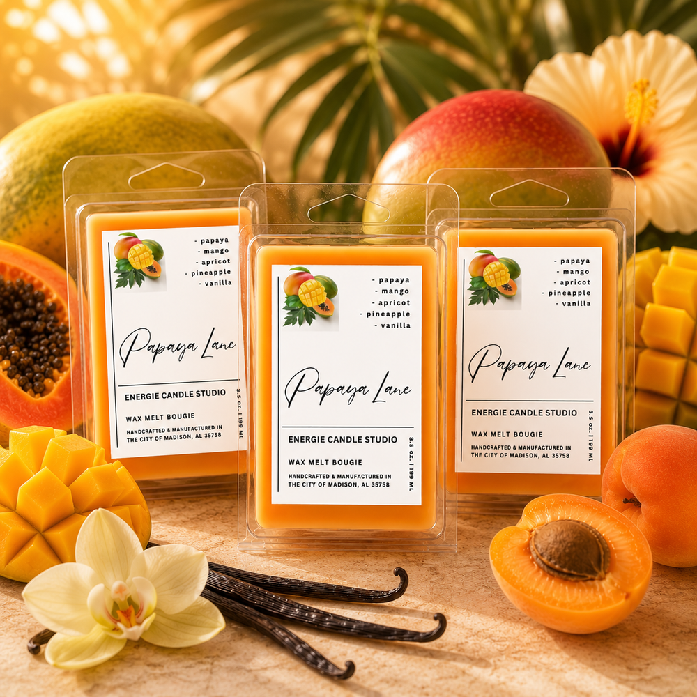 Three wax melt packages labeled 'Papaya Lane' by Energie Candle Studio are arranged on a wooden surface with tropical fruit, flowers, and vanilla beans around them. The packages are clear plastic with white labels showing yellow-orange wax samples and fruit illustrations.