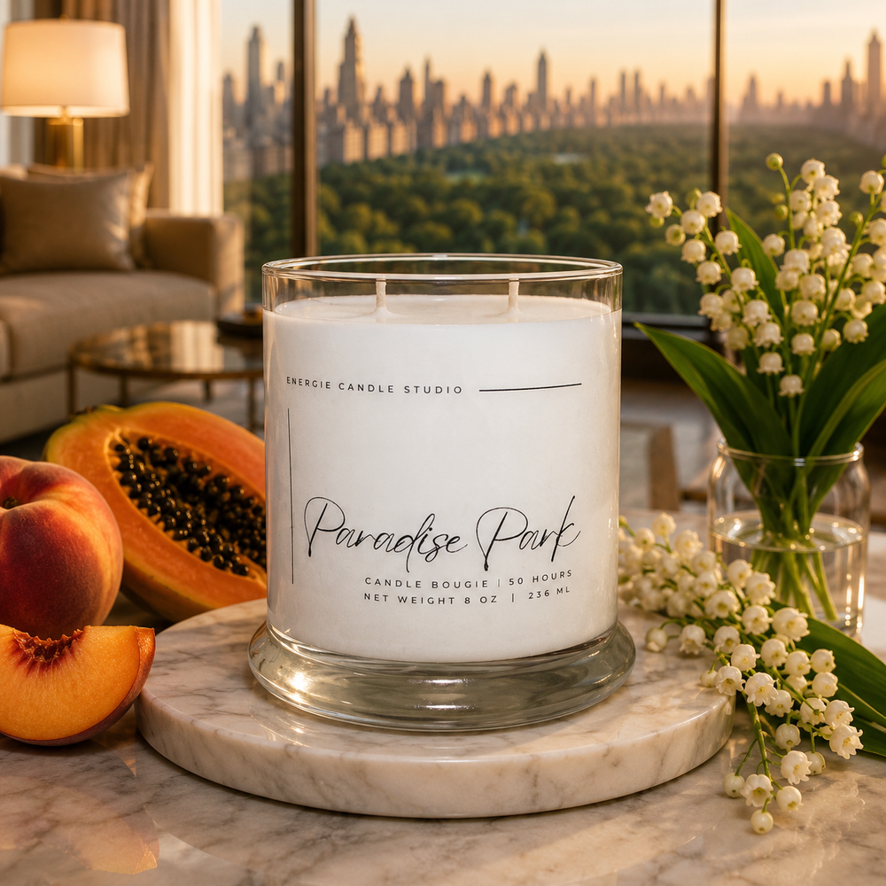 Candle labeled 'Paradise Park' on a marble surface with peaches and flowers, blurred cityscape in the background