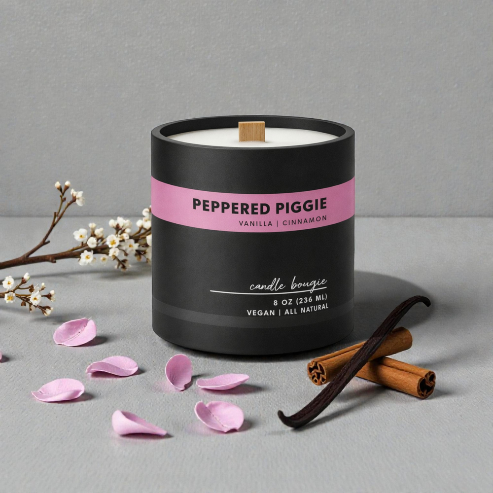 Candle labeled 'Peppered Piggie' with vanilla pod, cinnamon stick, and pink petals on a gray background