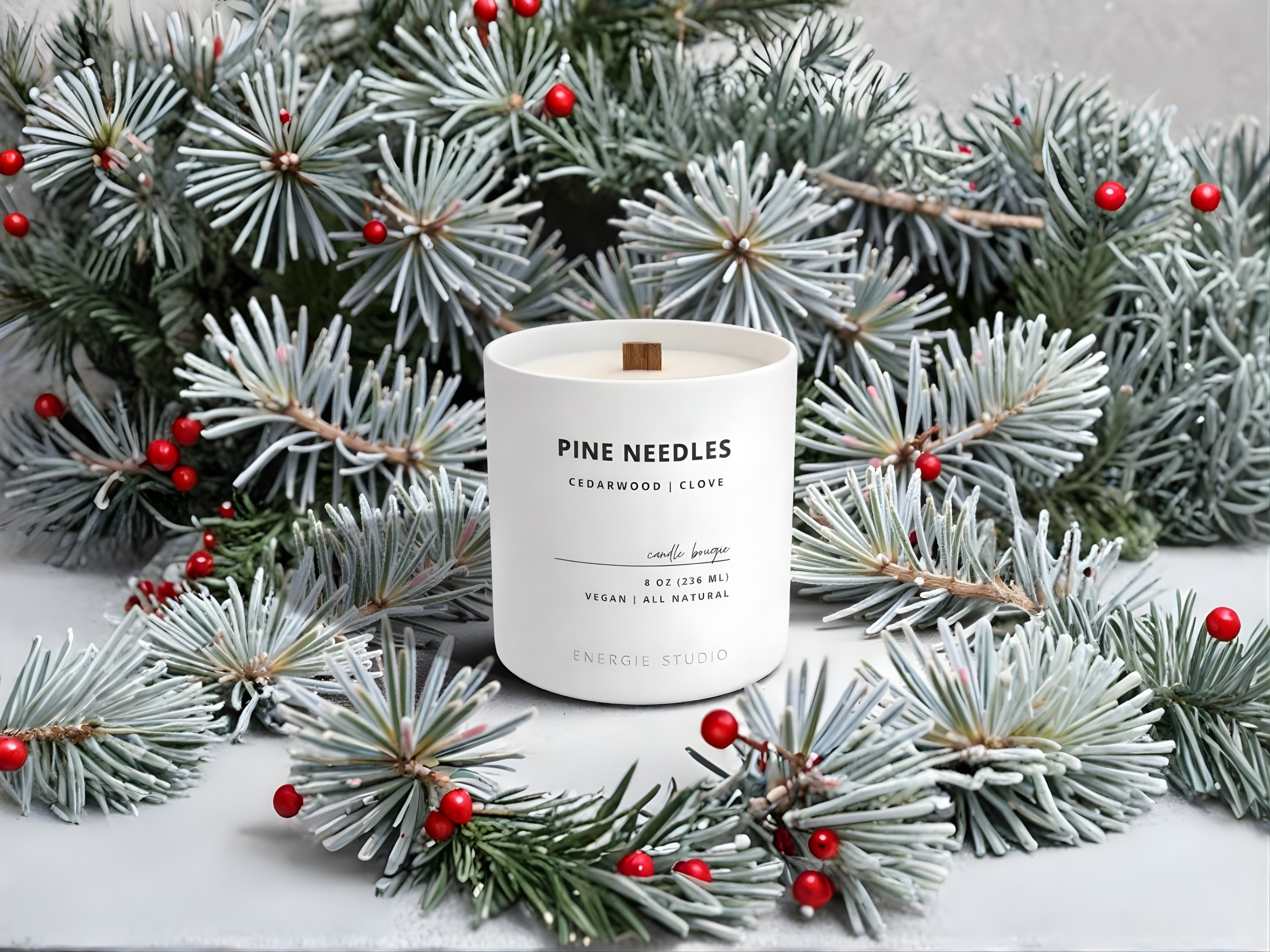 Candle labeled 'Pine Needles' surrounded by artificial Christmas trees with red berries on a light background