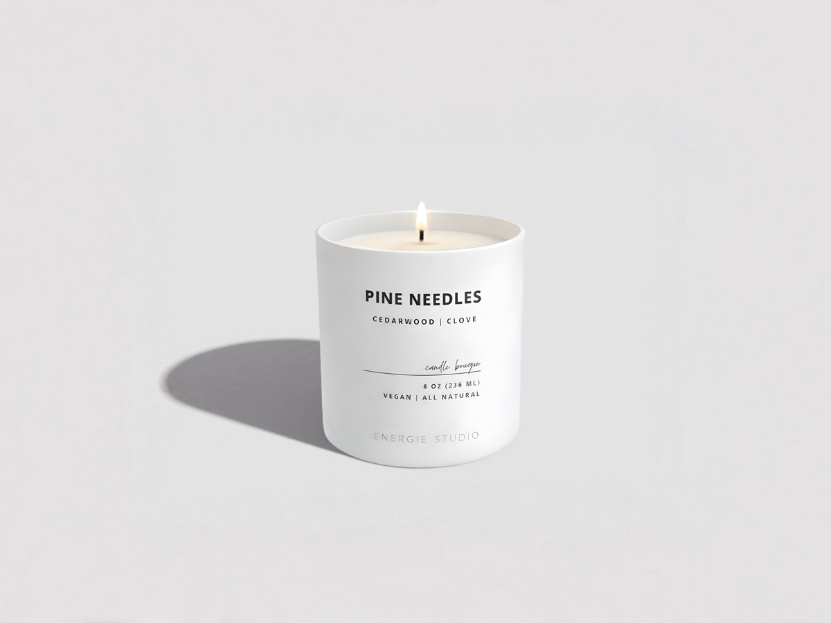 White candle with 'Pine Needles' label on a light gray background