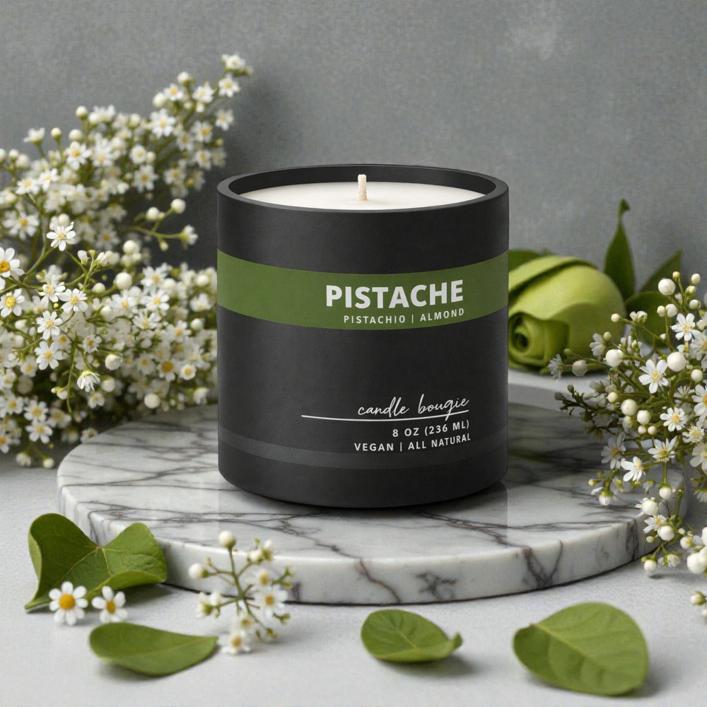 Candle with 'Pistache' label on a marble surface with flowers and leaves.