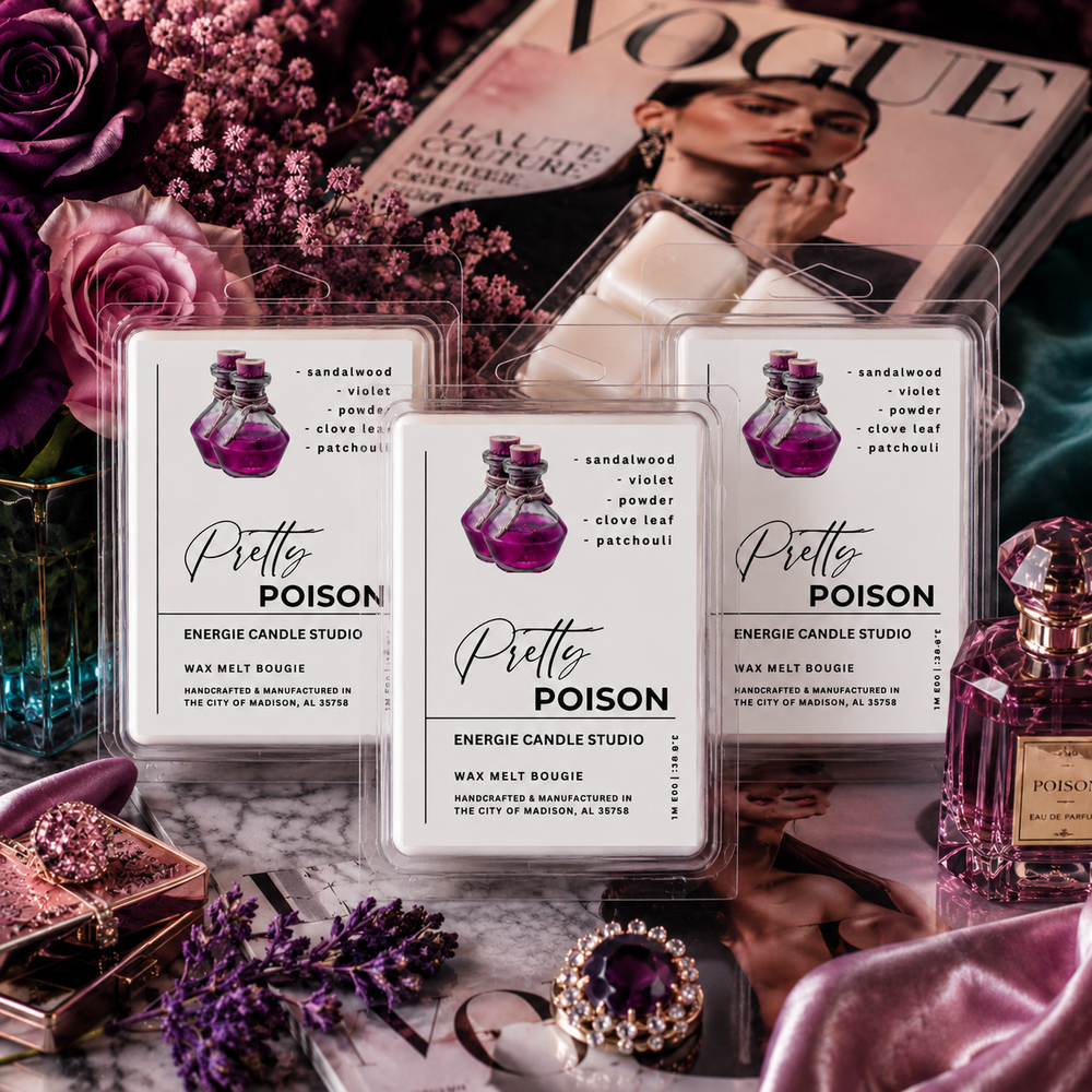 Three clear plastic clamshell packages of Pretty Poison Energize Candle Studio wax melts are arranged on a styled surface with roses, perfume bottles, jewelry, and a Vogue magazine in the background.