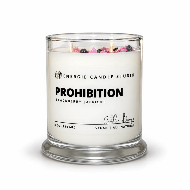 A 6 oz soy wax candle in a clear glass jar with a glass base, featuring a white label with black text that reads 'ENERGIE CANDLE STUDIO PROHIBITION BLACKBERRY | APRICOT'. The top of the candle is decorated with dried berries in pink, purple, and black.