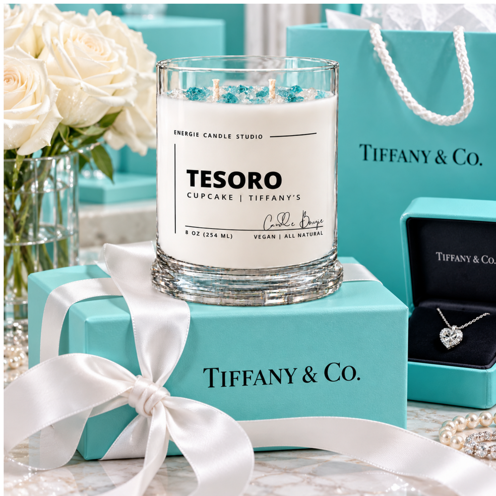 A Tiffany & Co. x Energie Candle Studio 'Tesoro Cupcake' scented candle in a clear glass jar with blue bead accents, styled with a turquoise gift box, white ribbon, a Tiffany shopping bag, a heart-shaped diamond necklace in a box, and white roses.