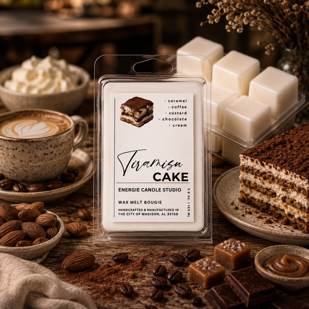 A clear plastic clamshell package labeled 'Tiramisu' wax melt by Energie Candle Studio sits on a rustic wooden table surrounded by coffee, whipped cream, almonds, cocoa powder, and a slice of tiramisu cake. A stack of white wax cubes is visible behind the package.