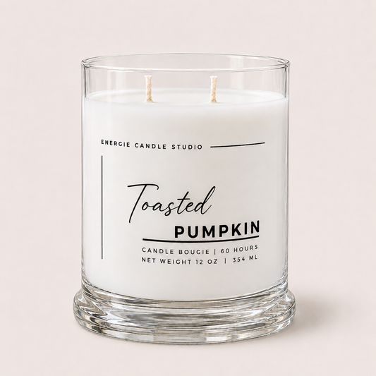 A two-wick scented candle in a clear glass jar with white wax, labeled 'Toasted Pumpkin' by Energie Candle Studio, set against a solid light beige background.