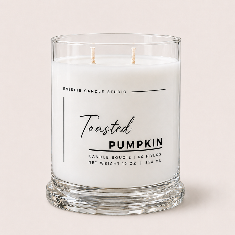A two-wick scented candle in a clear glass jar with white wax, labeled 'Toasted Pumpkin' by Energie Candle Studio, set against a solid light beige background.