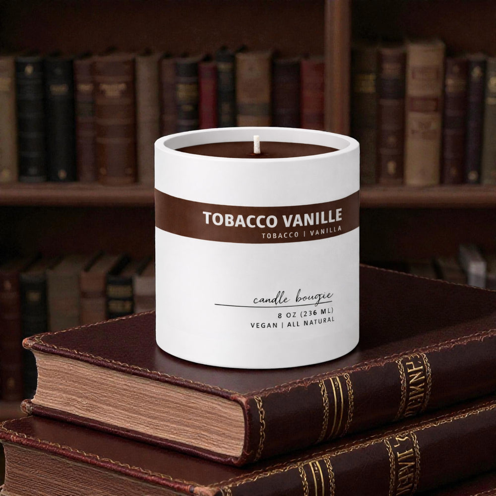 Candle labeled 'Tobacco Vanille' on a stack of books with a bookshelf background