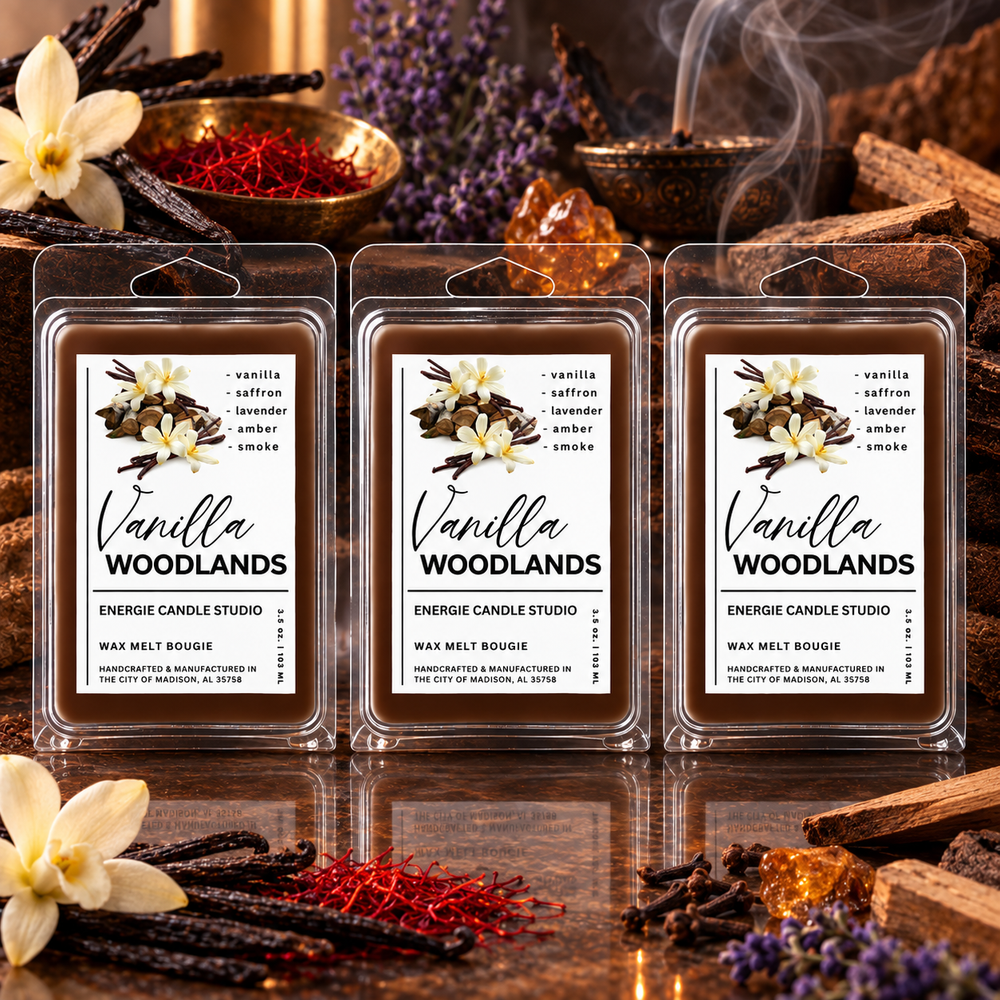 Three packaged wax melts labeled Vanilla Woodlands are arranged on a reflective surface with warm decorative props including flowers, cinnamon sticks, a bowl of red spice, and a copper mug with steam. The product packaging is clear plastic clamshell with a white label featuring vanilla and saffron illustrations.