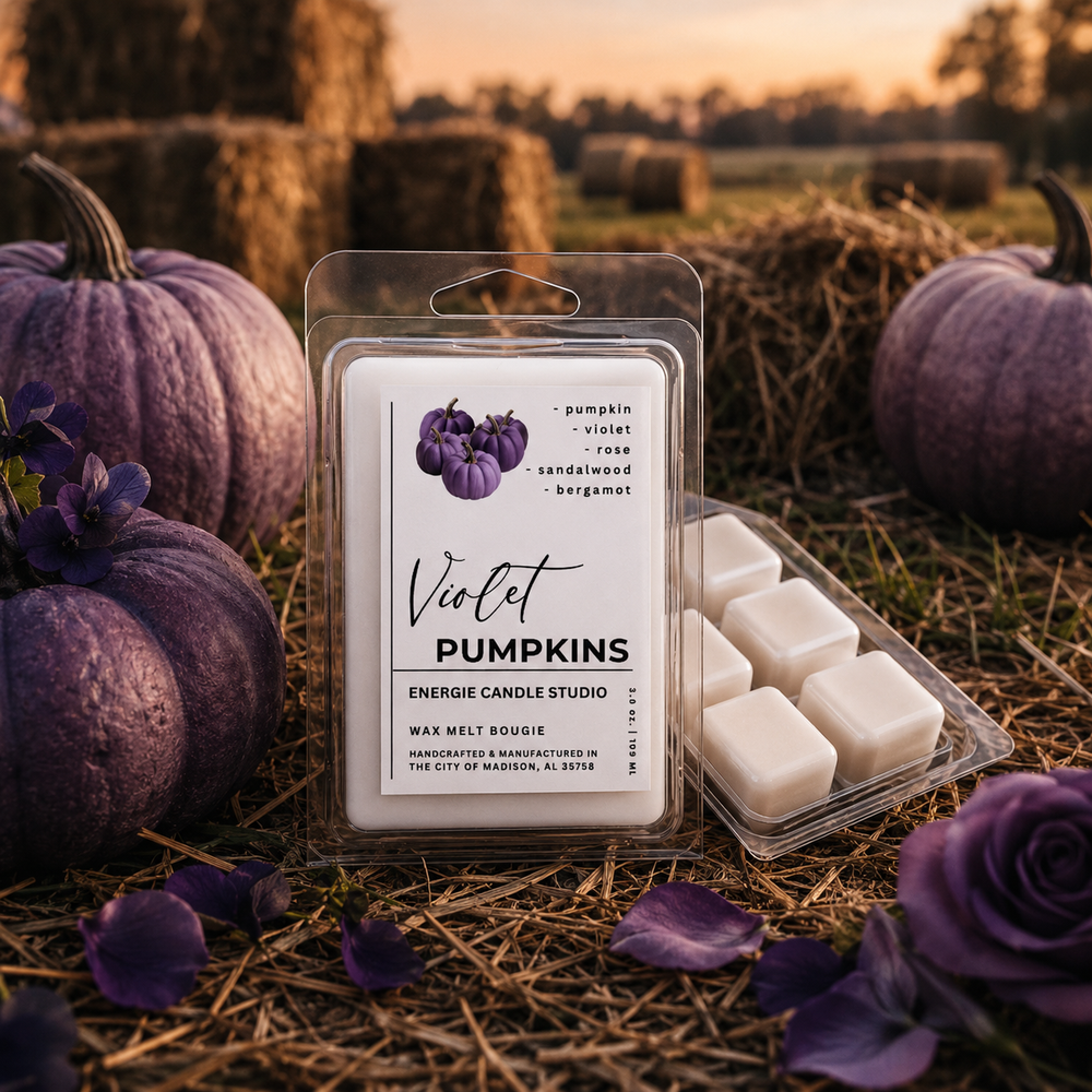 A package of wax melt scents labeled 'Violet Pumpkins' by Energie Candle Studio, displayed next to loose wax melts in a clear plastic tray. The scene is styled with purple pumpkins, purple roses, and straw bales in an outdoor hayfield at sunset.