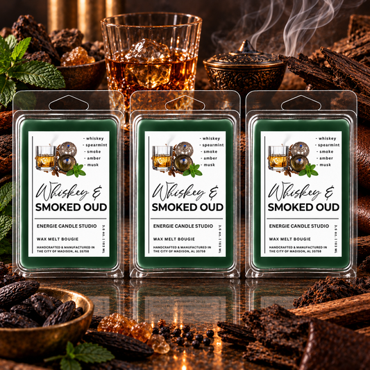 Three packaged wax melts labeled 'Whiskey & Smoked Oud' are displayed in front of a warm, rustic background with whiskey glasses, wood, and spices. The wax melts are in clear plastic clamshell packaging with green labels featuring white text and an illustration of a whiskey glass with ice and spices.
